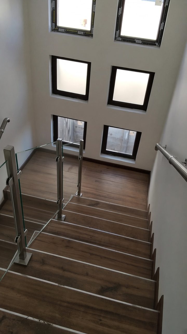 Escalera en U con peldaños de madera, pilares de acero inoxidable con pinzas y paneles de vidrio templado, vista desde arriba